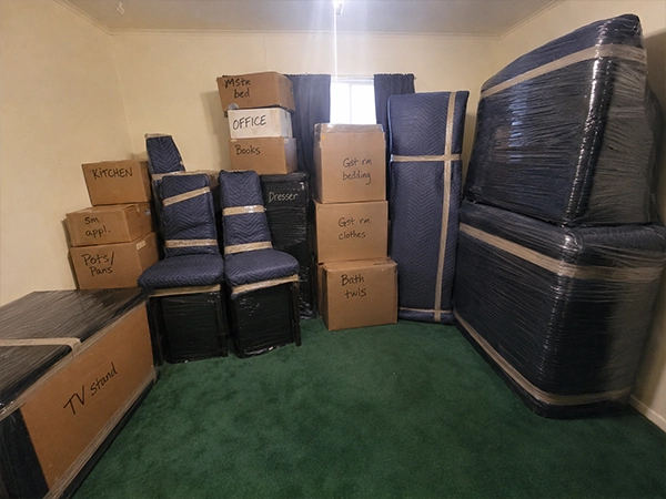 A room of cartons labeled by room alongside wrapped furniture and mattresses ready to load