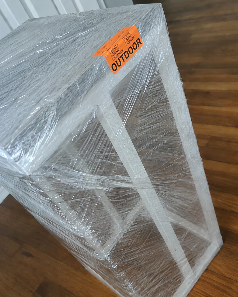 A console table wrapped in stretch film with an orange inventory tag taped to the top