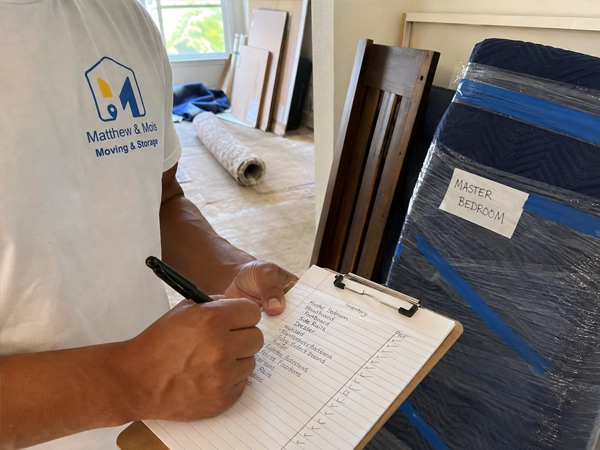 A crew member writing an inventory sheet on a clipboard beside a blanket-wrapped piece labeled for the master bedroom